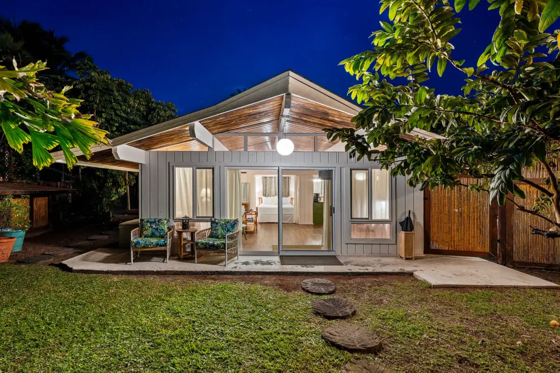 A modern house at night with a bright glass-fronted living area and a small lawn.