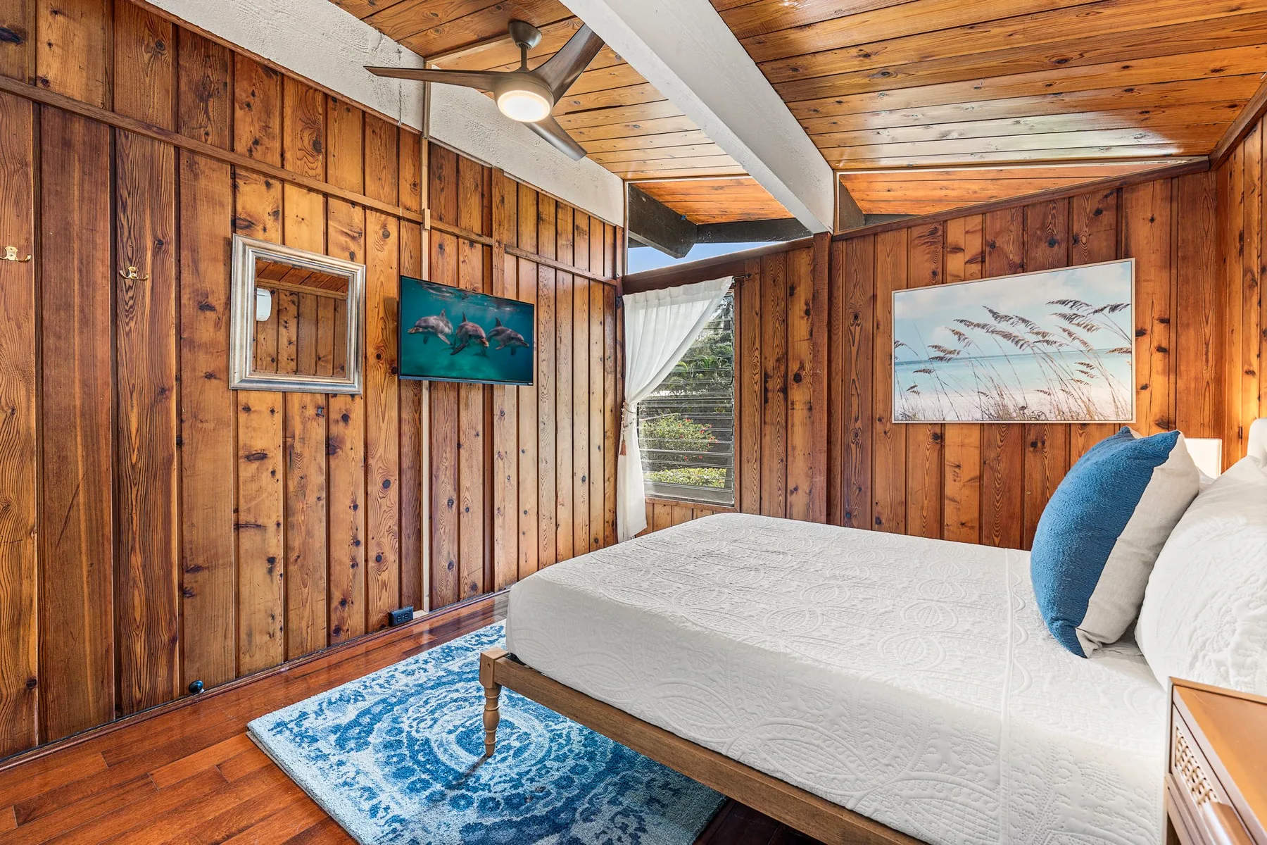 A wood-paneled bedroom with a bed and a blue patterned rug.