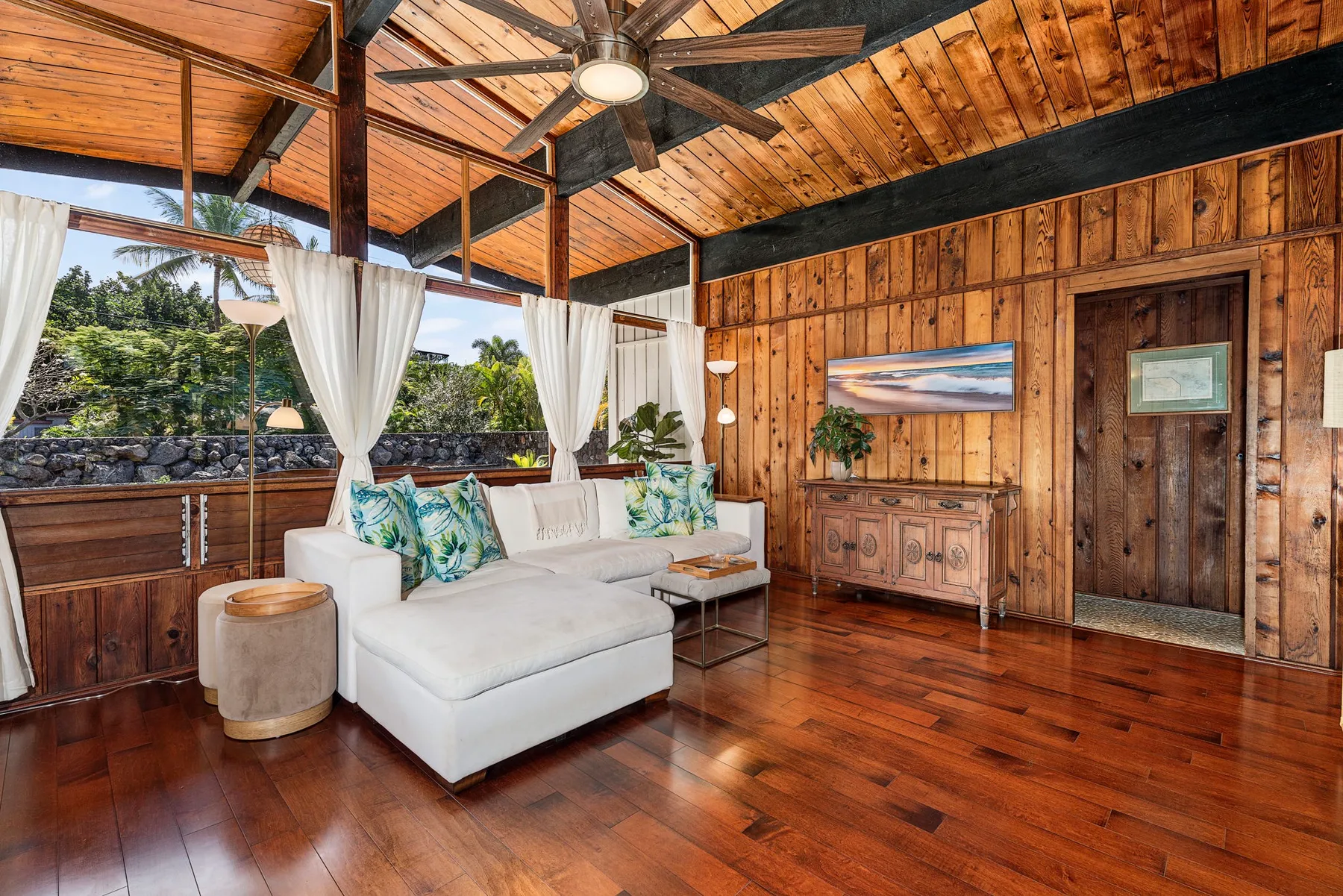 A wood-paneled living room with a white sectional sofa and large windows.