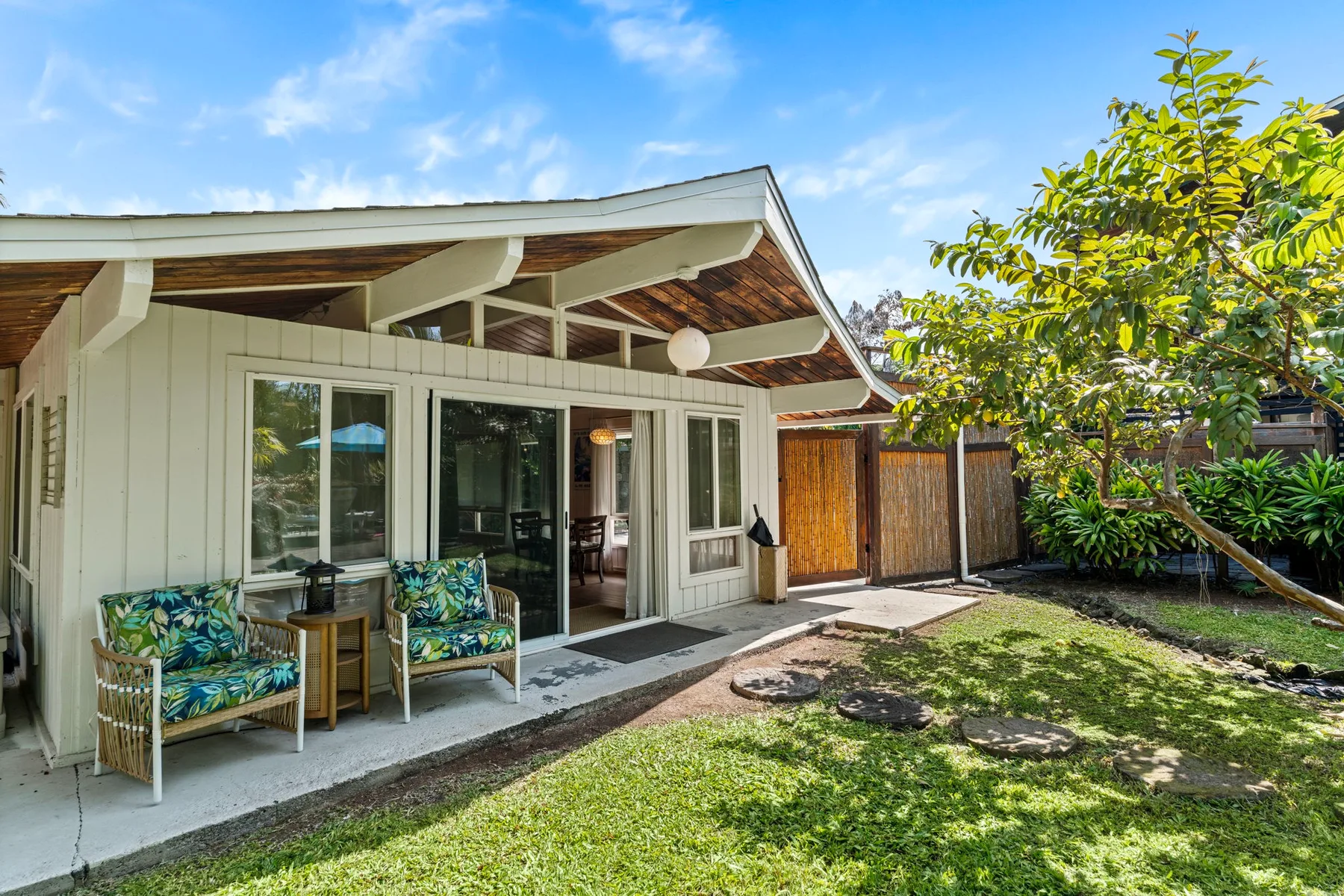 A patio with outdoor seating overlooks a grassy yard beside a white building.