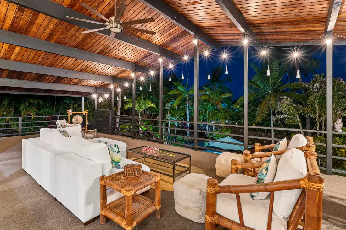A covered outdoor lounge has cushioned seating beneath a wooden slatted roof.