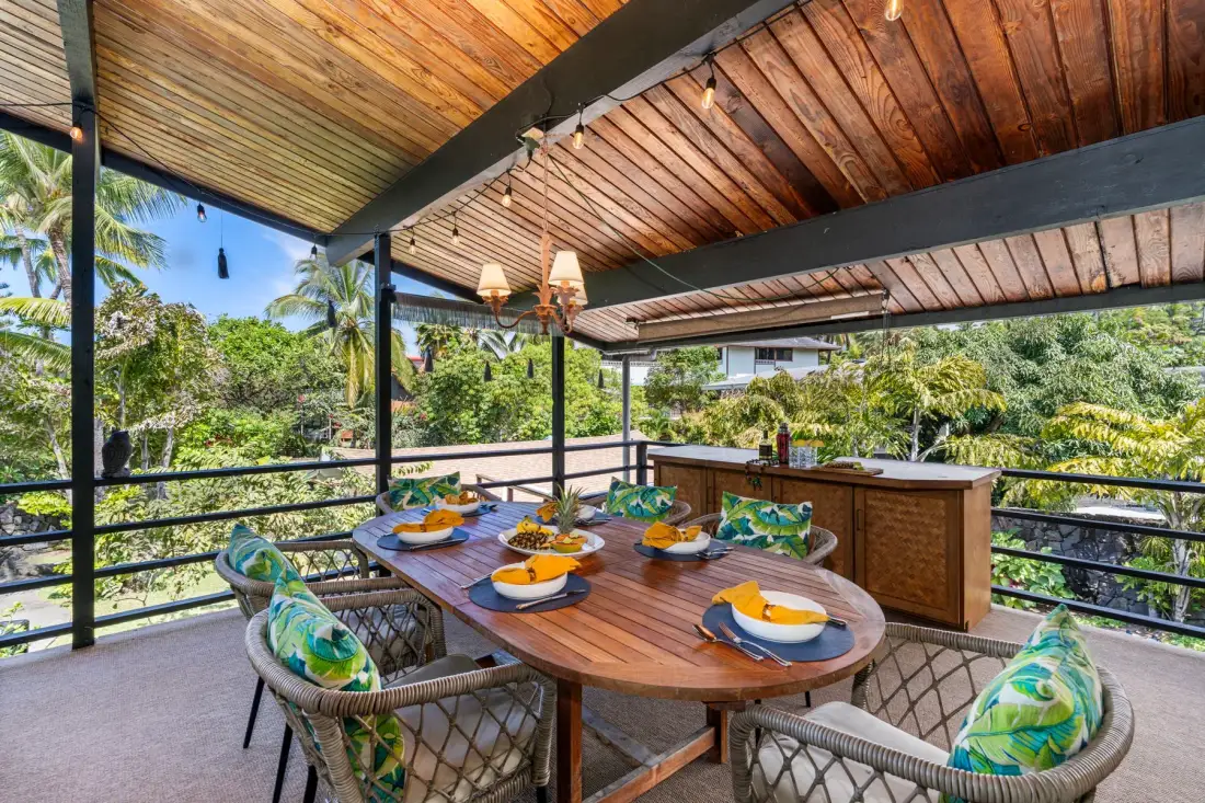 A covered outdoor dining area with a wooden table and surrounding greenery.