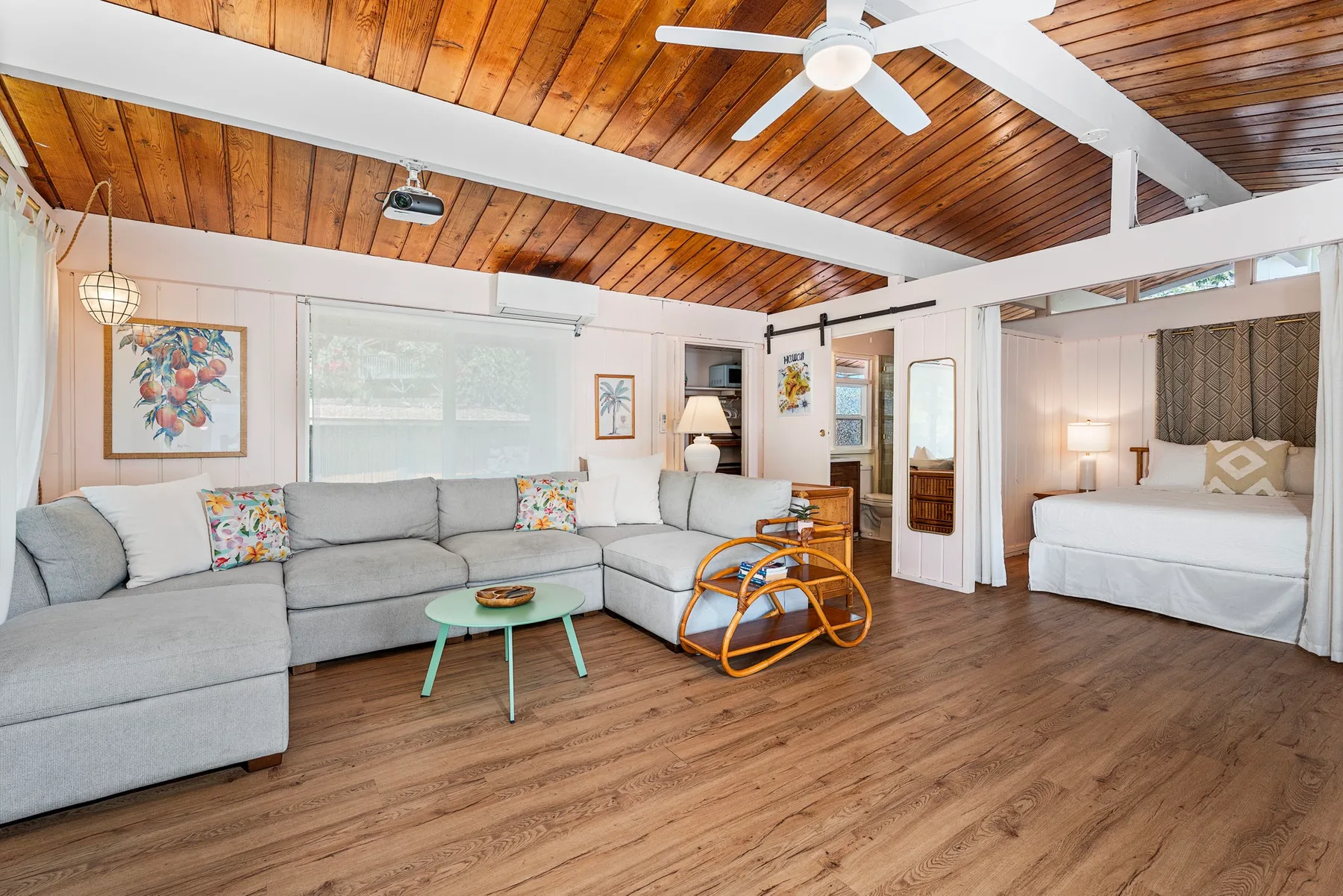 A bright living area with a sectional seating arrangement and a bed in an adjoining space.