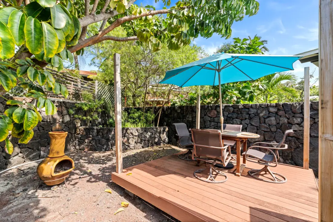 An outdoor patio with a table and chairs beneath a turquoise umbrella.