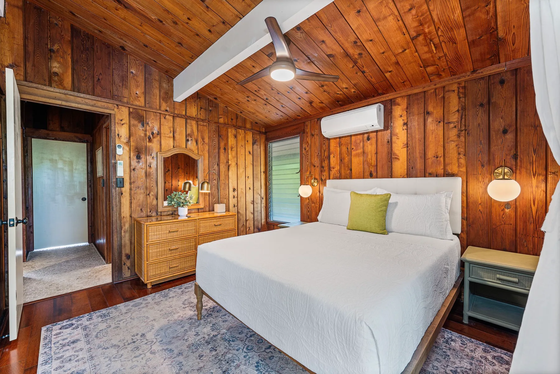 A bedroom with a neatly made bed, wood-paneled walls, and a ceiling fan.