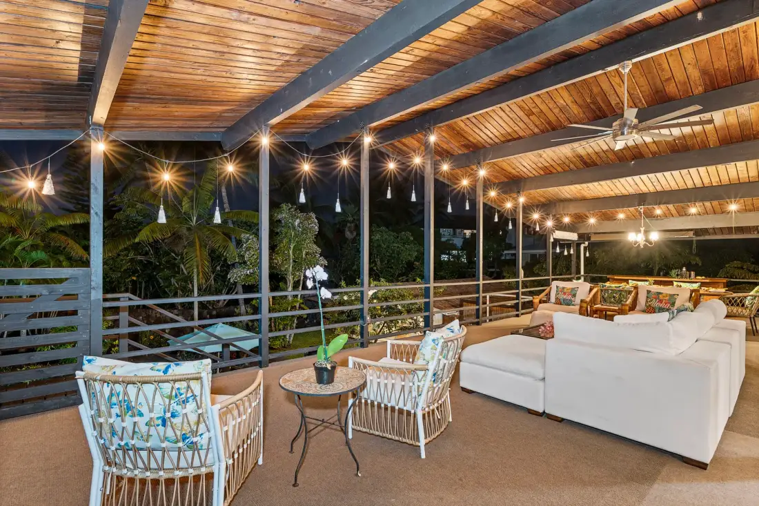 A covered outdoor seating area with string lights and views of greenery.