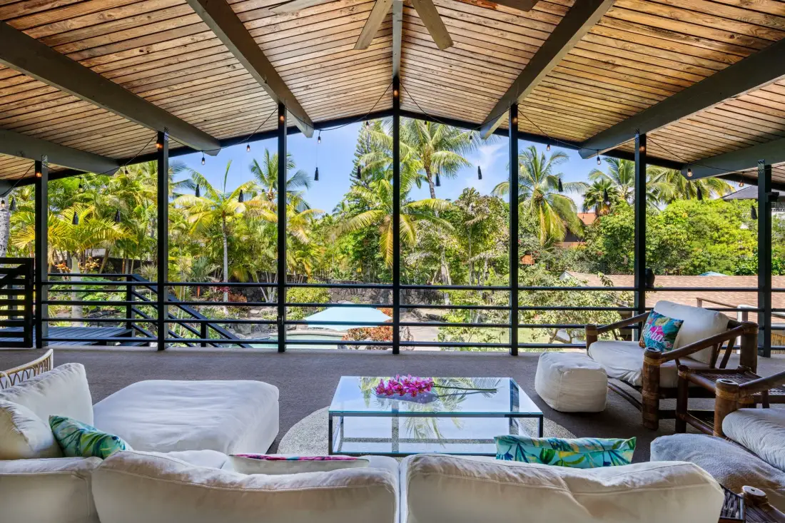 An open-air lounge with seating and a glass table overlooks palm trees.