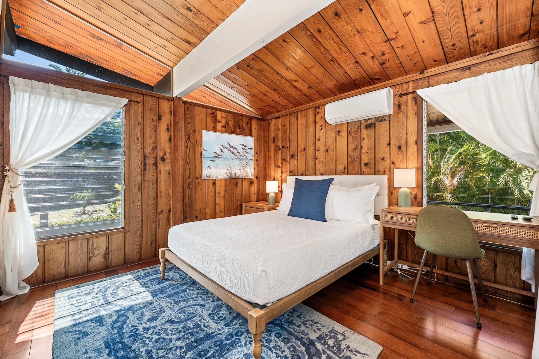 A wood-paneled bedroom with a bed, large windows, and a blue rug.