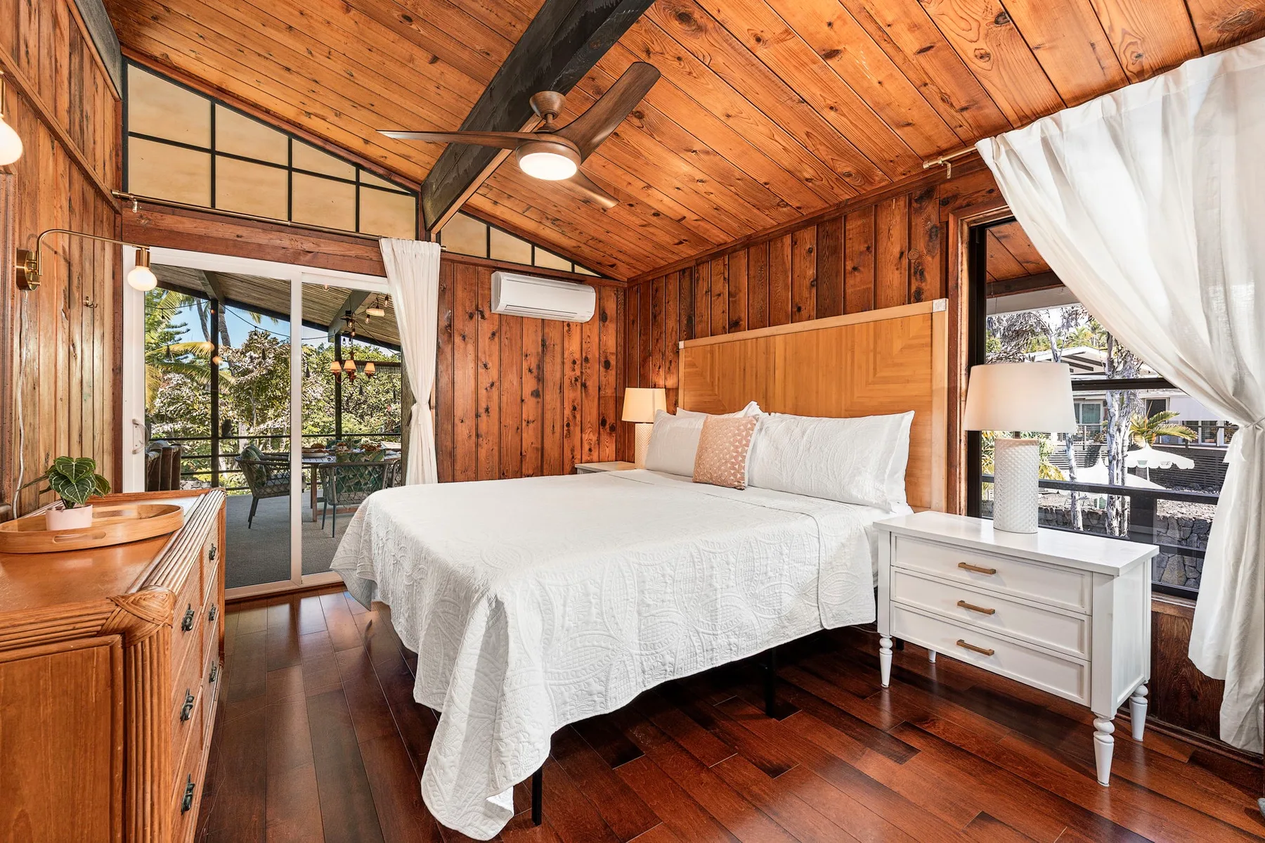A bedroom with a white bed, wood-paneled walls, and a sloped wooden ceiling.