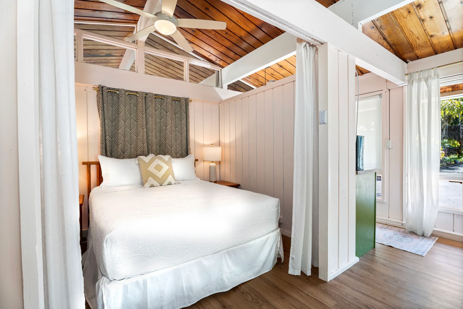 A bedroom with a bed beneath a wooden ceiling and ceiling fan.