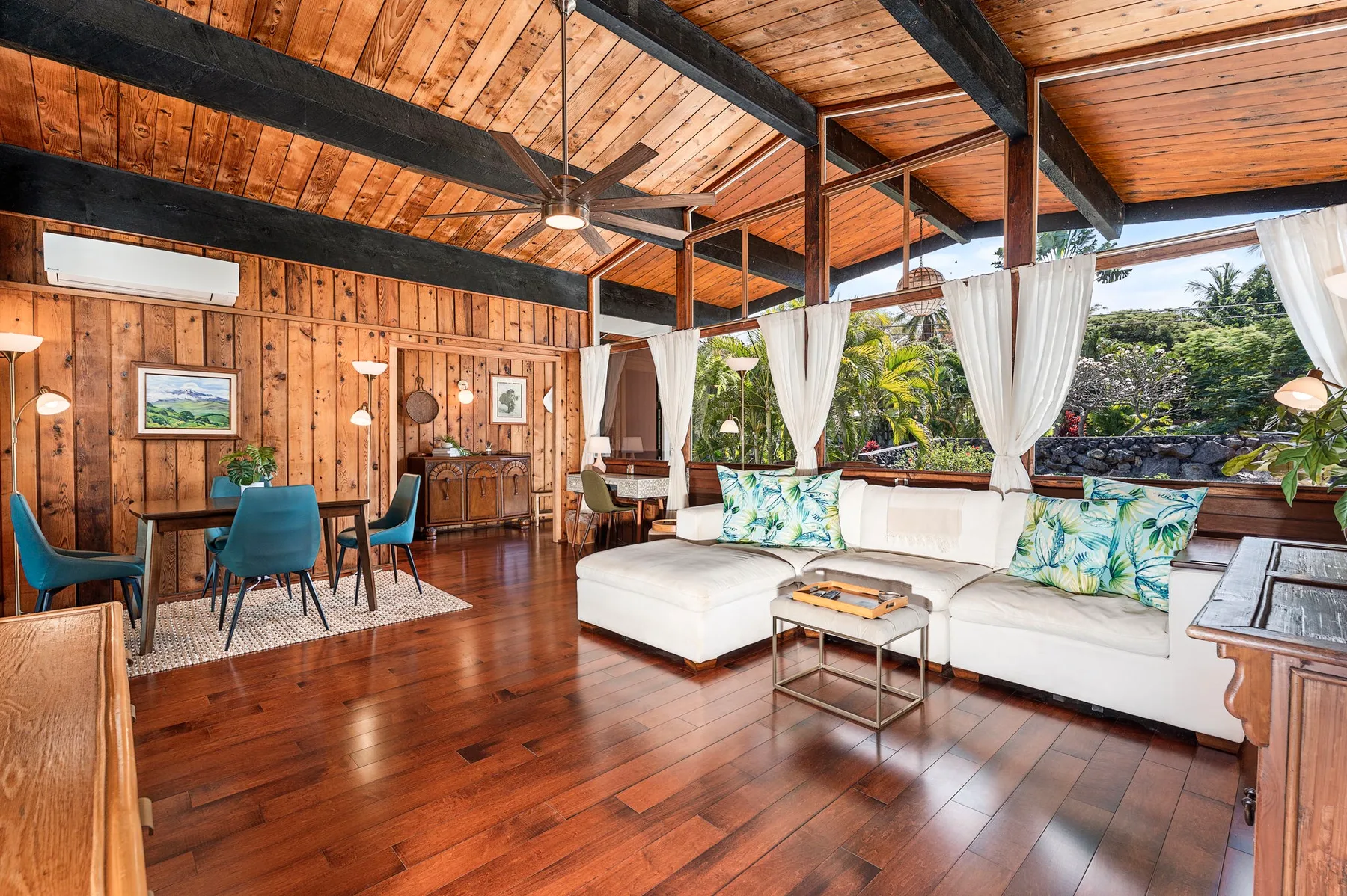 A wood-paneled living room with white seating and large windows overlooking greenery.