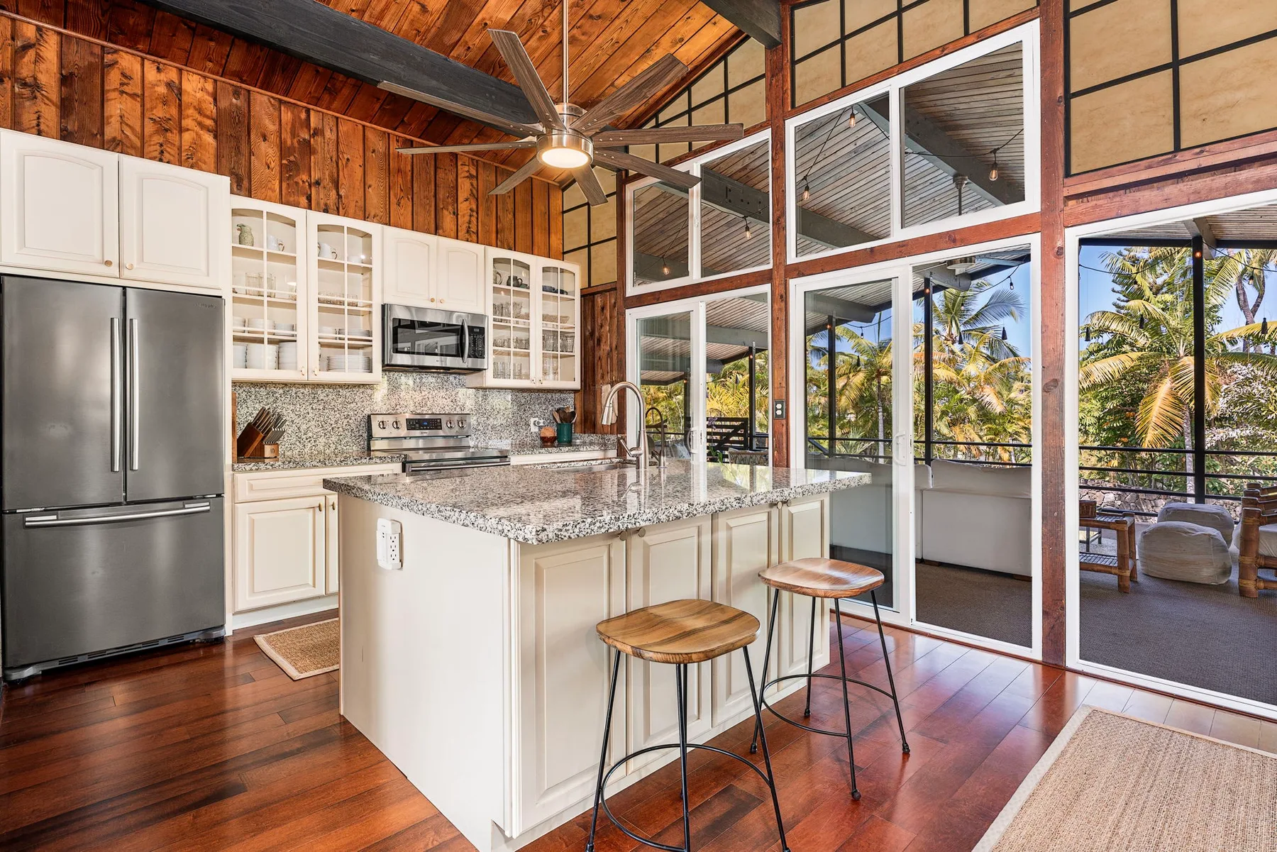 A kitchen with a central island and large windows overlooking palm trees.