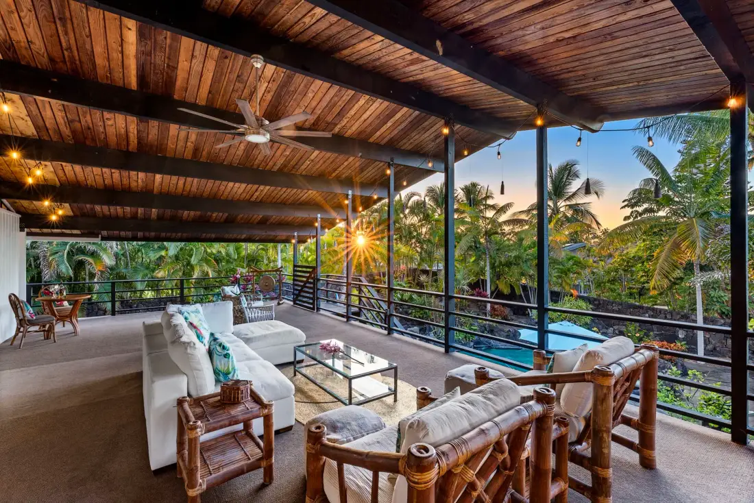 A covered outdoor lounge with seating and views of tropical greenery.