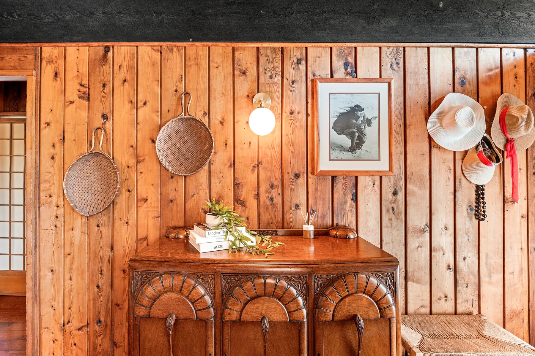 A wood-paneled room with a decorated console table and hats hanging on the wall.