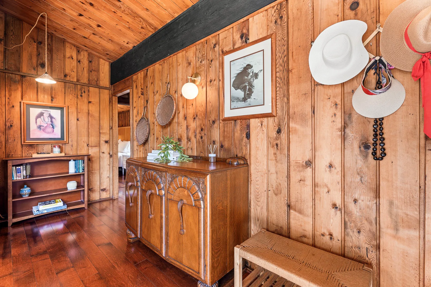 A wood-paneled room with a wooden cabinet, framed art, and hats hanging on the wall.