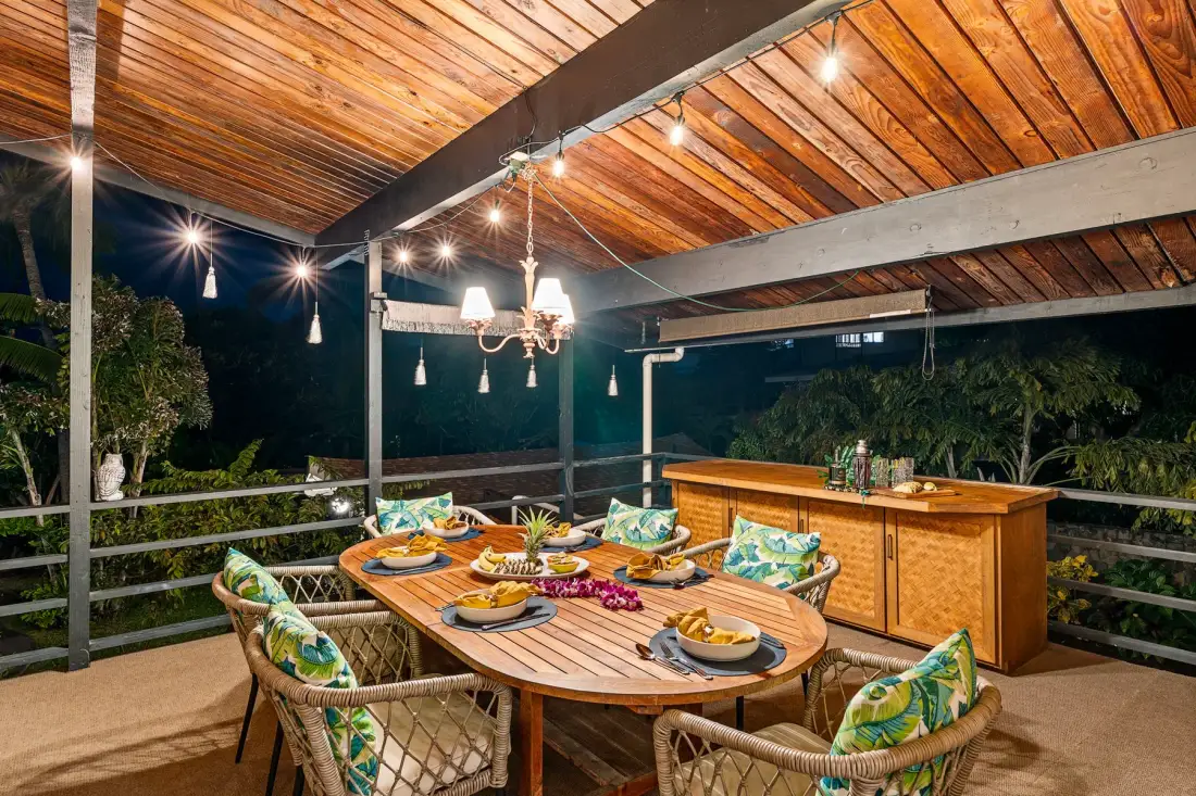 A covered outdoor dining area with a wooden table and surrounding greenery.