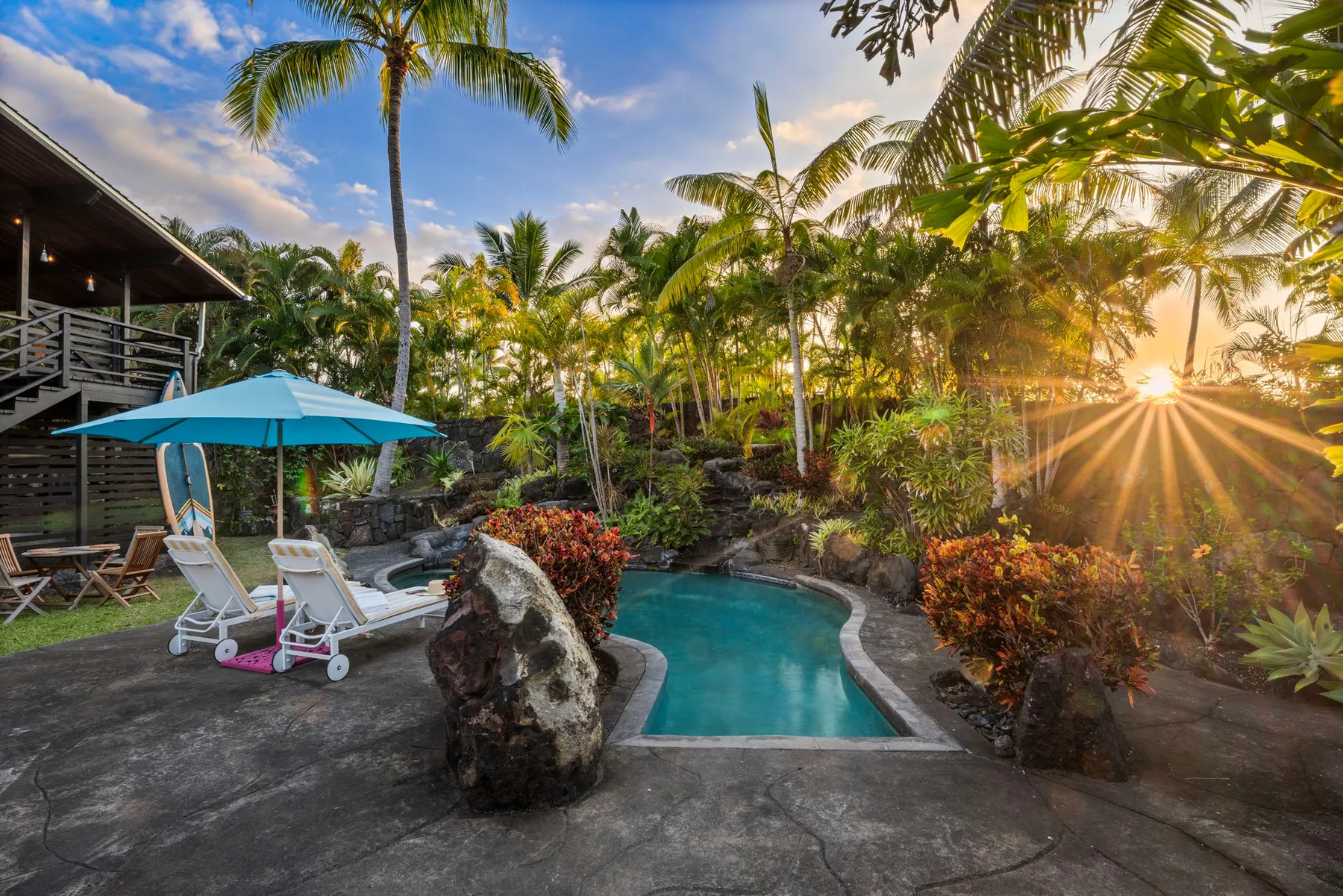 An outdoor pool sits among tropical plants beside a shaded seating area.