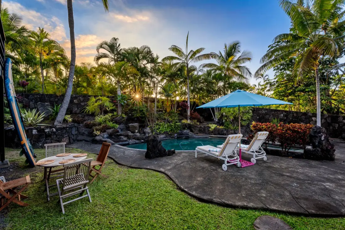 A tropical pool area with lounge seating beneath a blue umbrella.