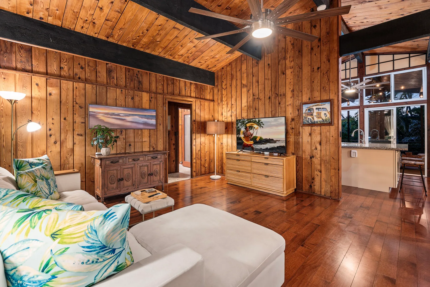 A wood-paneled living room with seating, a ceiling fan, and an open kitchen area.