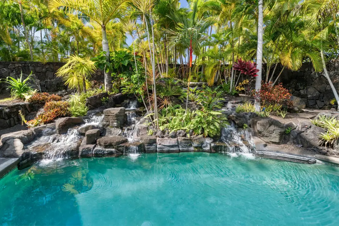 A tropical swimming pool bordered by rocks, greenery, and small waterfalls.