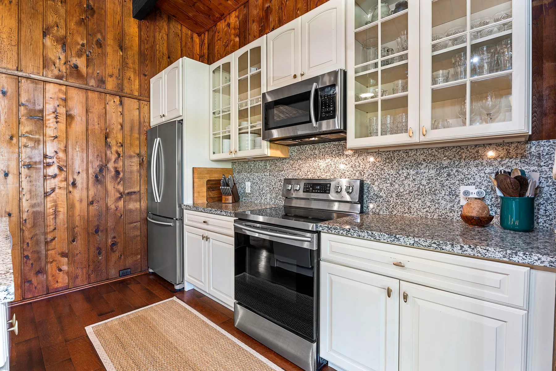 A kitchen with white cabinets, stainless steel appliances, and wood-paneled walls.