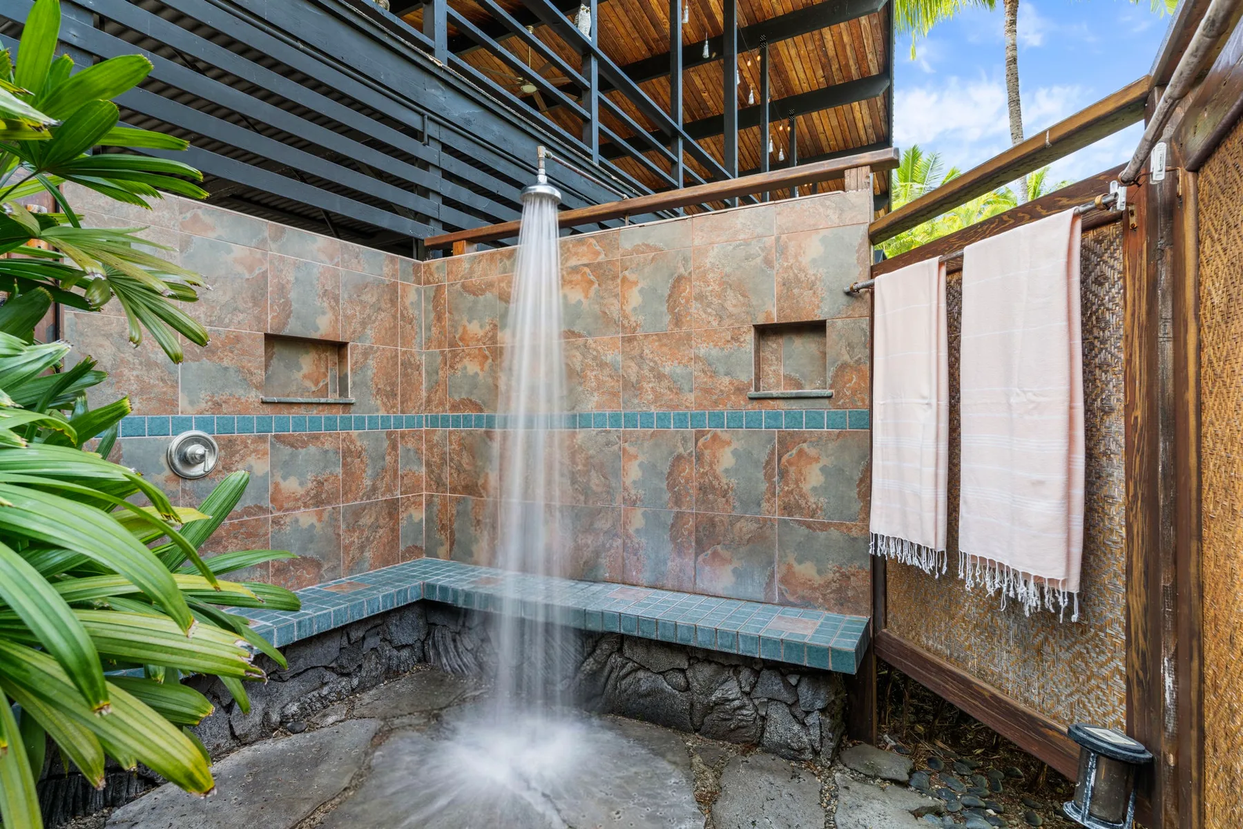 An outdoor shower area with tiled walls and towels hanging nearby.