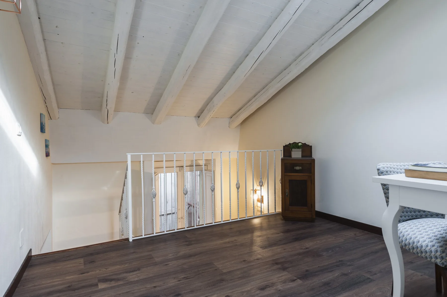 Un rellano interior elevado con barandilla blanca y suelo de madera oscura.
