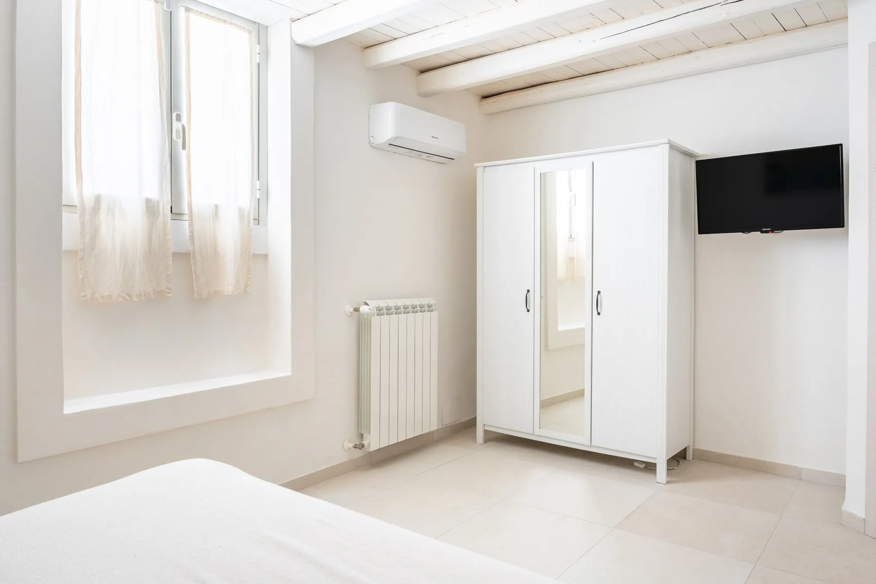 Un dormitorio luminoso con un armario blanco y un televisor en la pared.