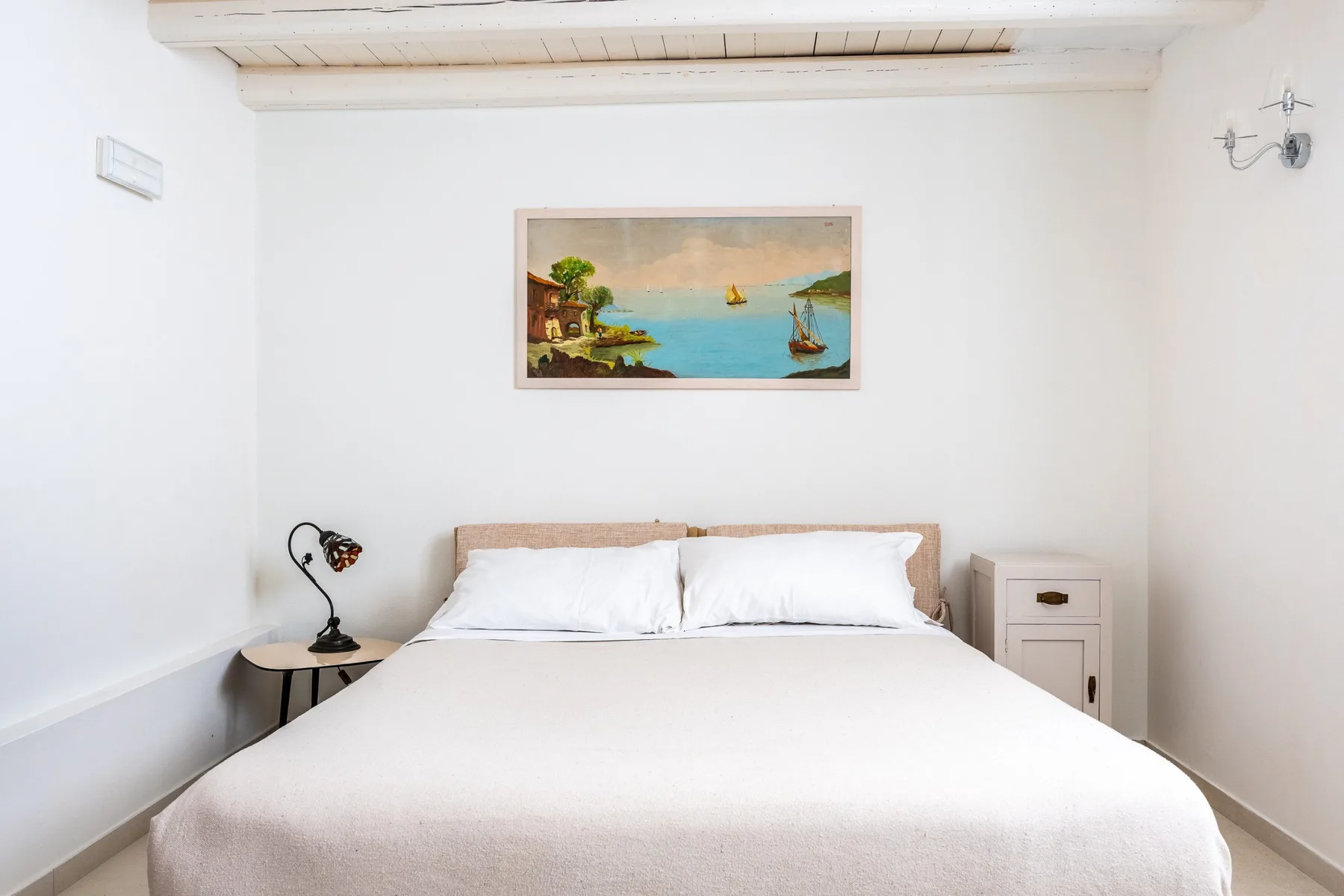 Un dormitorio con una cama bajo un cuadro enmarcado de una escena costera.