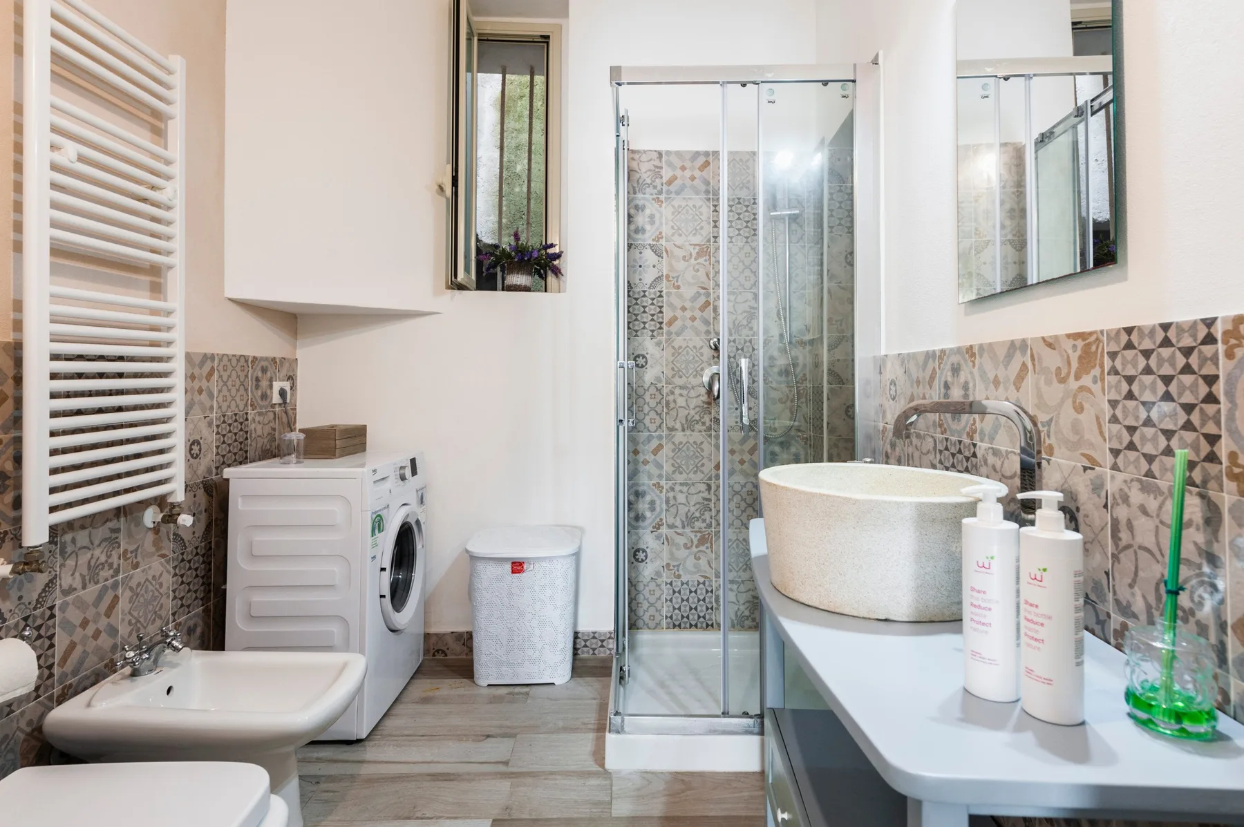 Un baño con ducha de vidrio, lavabo y azulejos estampados en las paredes.
