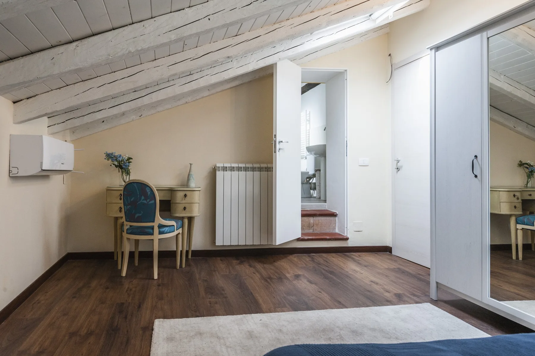 Un dormitorio con un pequeño escritorio, una silla y una puerta hacia el baño.