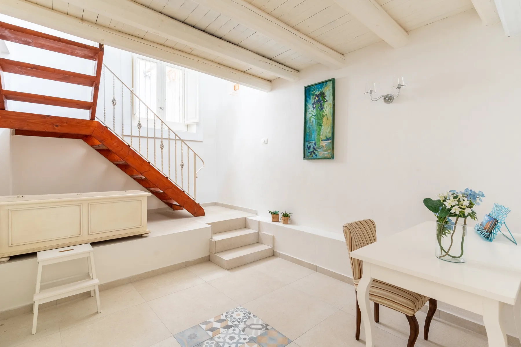 Una habitación luminosa con una escalera de madera y muebles blancos.