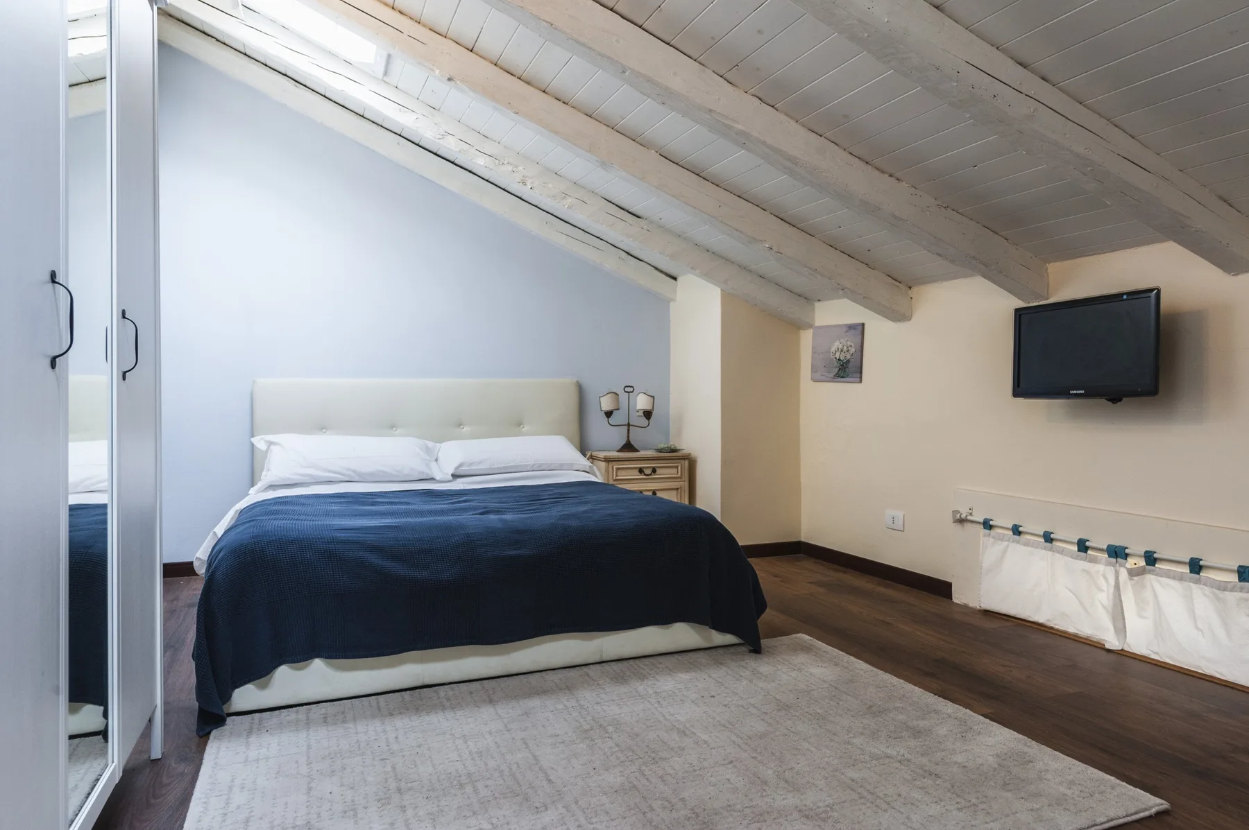 Un dormitorio con una cama bajo un techo inclinado y un televisor en la pared.