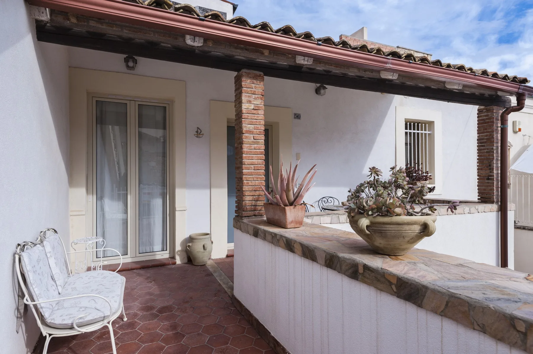 Un patio exterior cubierto con suelo de baldosas y plantas en macetas.