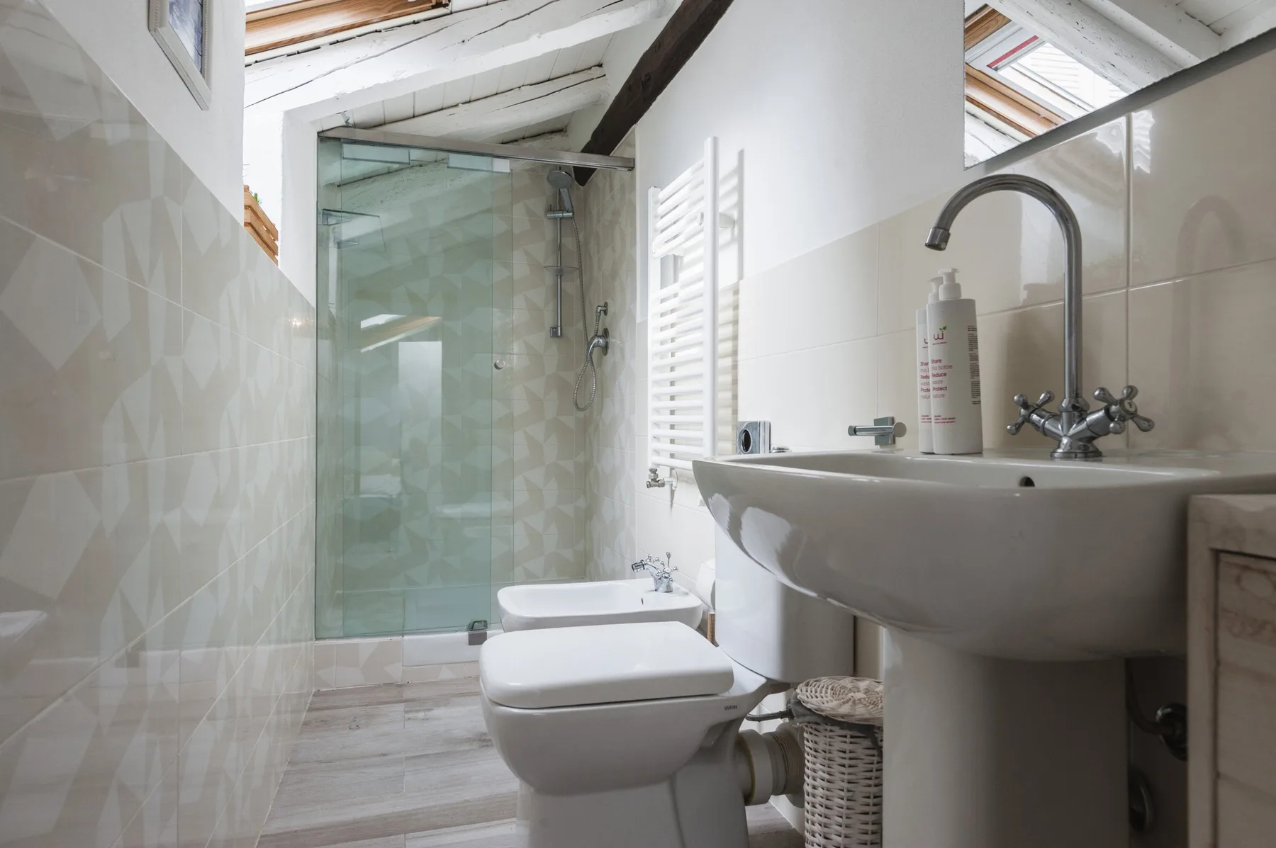 Un baño luminoso con ducha de vidrio, inodoro y lavabo con pedestal.