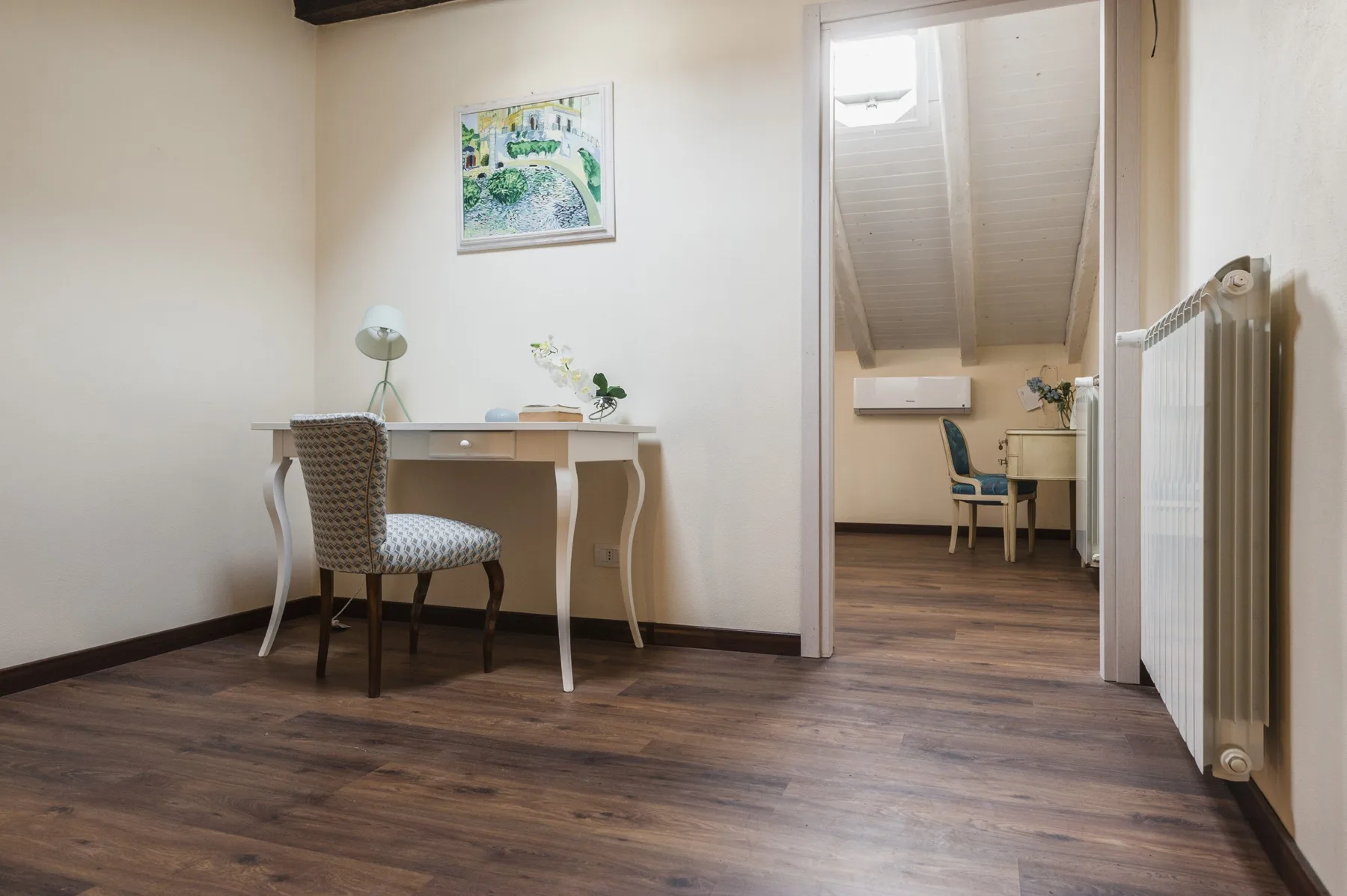 Un escritorio y una silla están en una habitación luminosa con una zona de trabajo contigua.