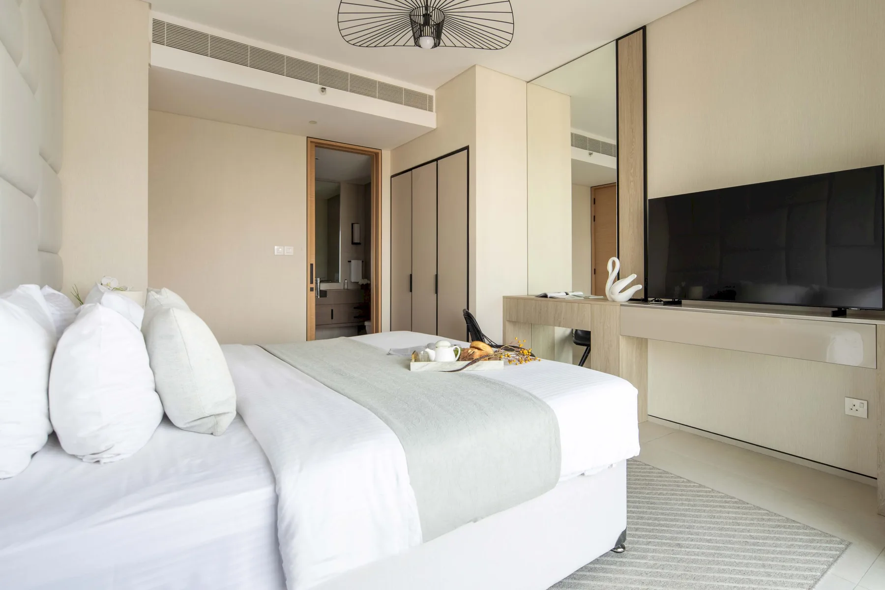 Un dormitorio luminoso con una cama grande y un televisor montado en la pared.