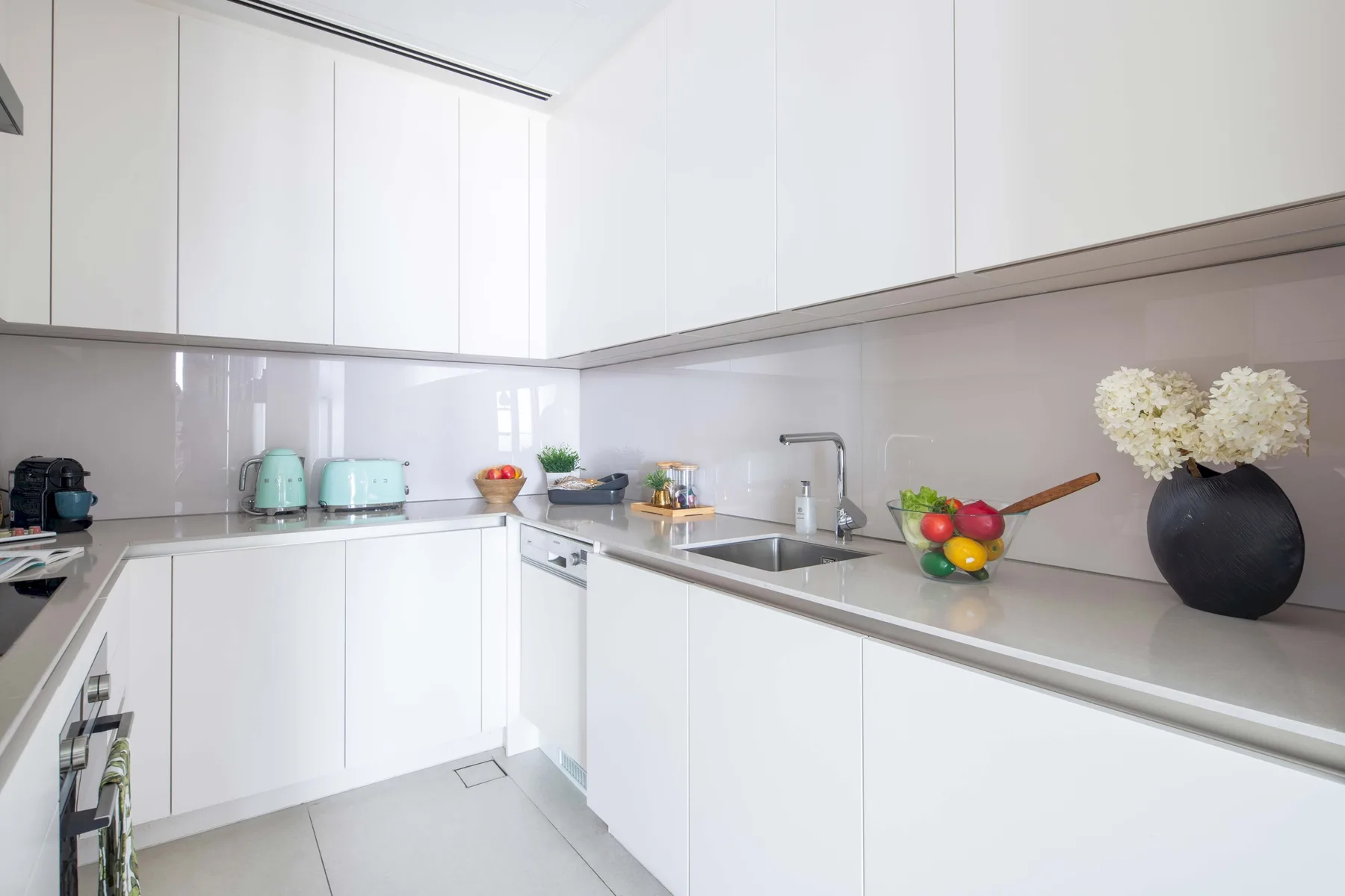 Una cocina moderna y luminosa con gabinetes blancos, electrodomésticos de encimera y fregadero.