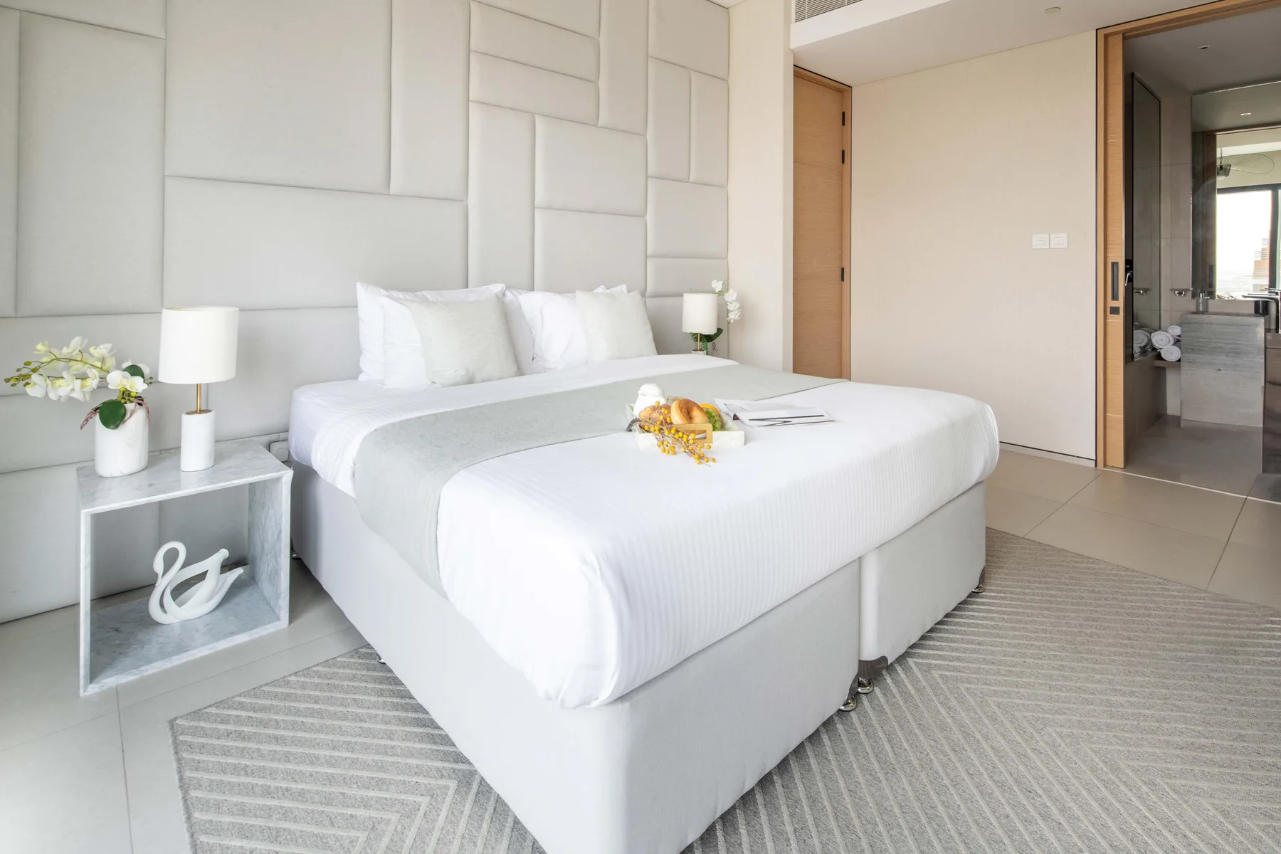 Un dormitorio luminoso con una cama tendida y una pared con paneles geométricos.