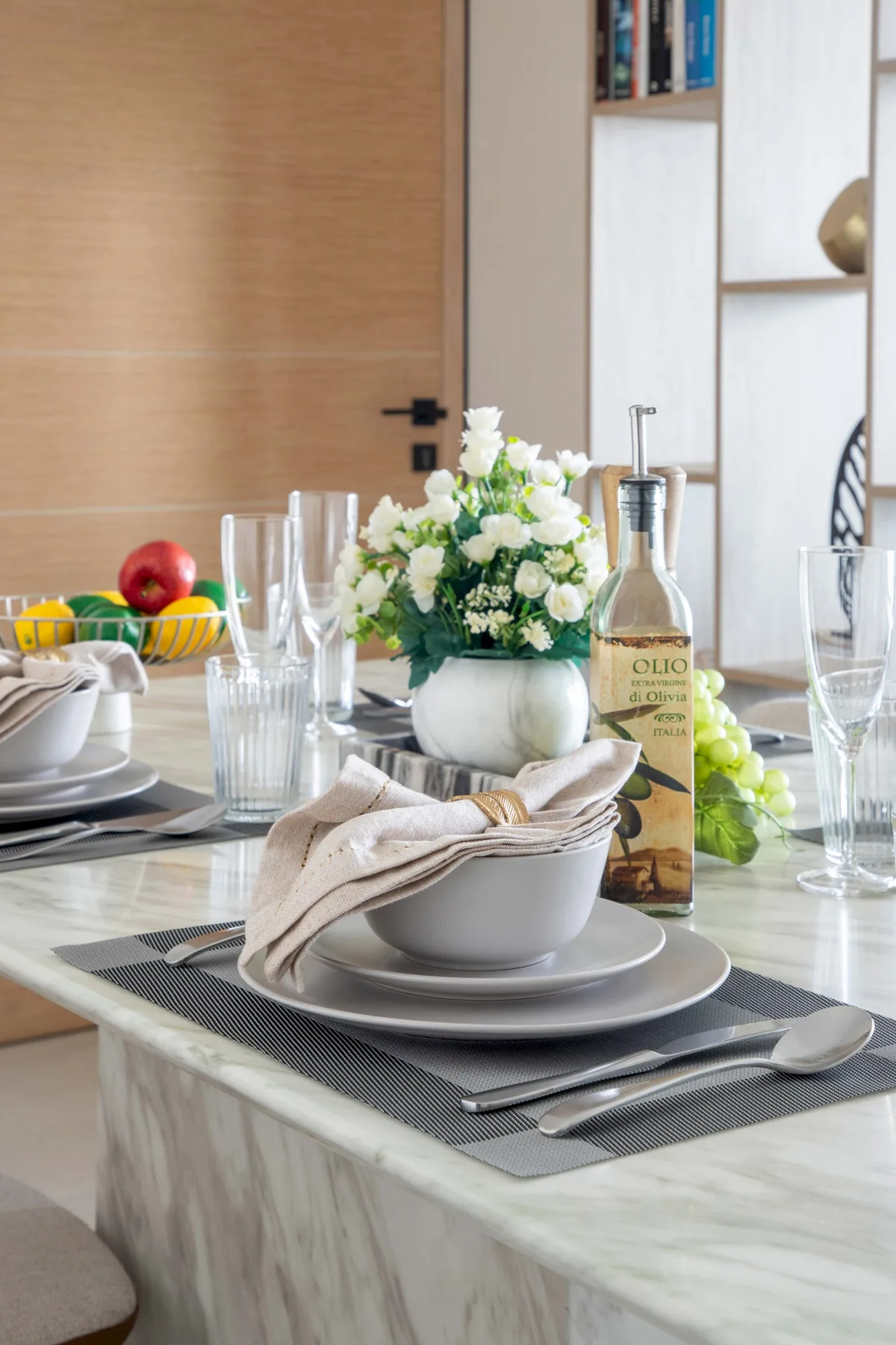 Una mesa de comedor está puesta con platos, vasos, fruta y un arreglo floral.