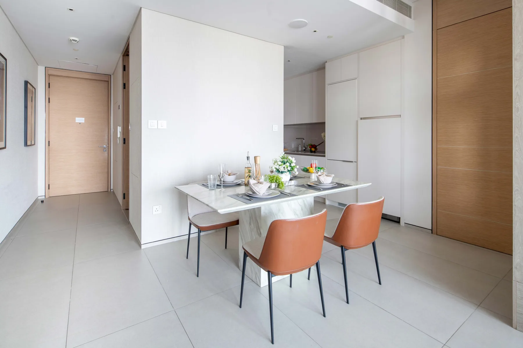 Un comedor luminoso con la mesa puesta y asientos naranjas junto a la cocina.