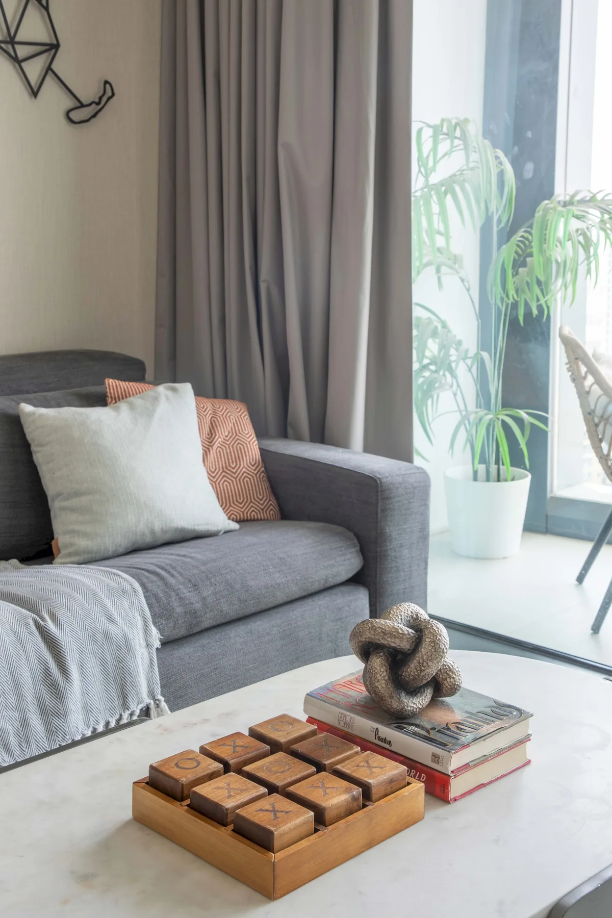 Una sala de estar con un sofá gris junto a una ventana luminosa y plantas en macetas.