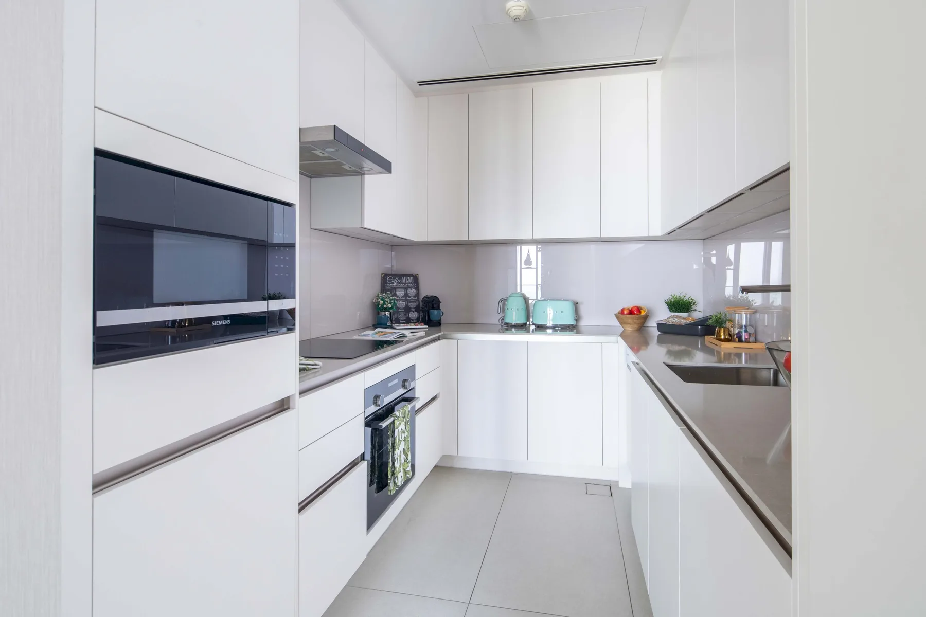 Una cocina blanca y luminosa con electrodomésticos integrados y una encimera de acero inoxidable.