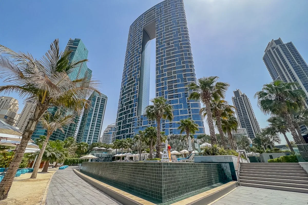 Una zona de piscina al aire libre con jardines se encuentra junto a edificios modernos de gran altura.