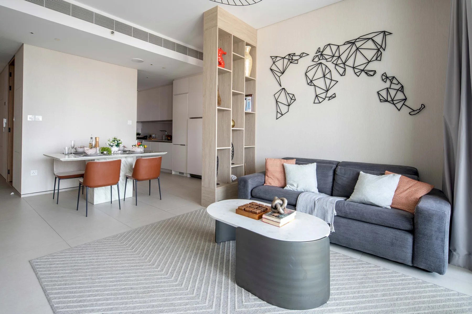 A living room with a gray sofa and a dining area beside the open kitchen.