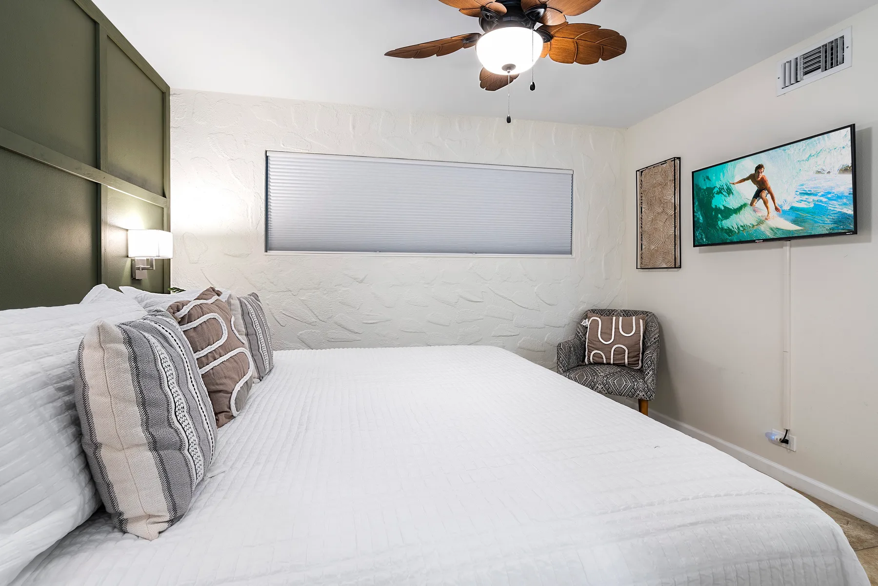 Un dormitorio con una cama grande, almohadas estampadas y un televisor en la pared.