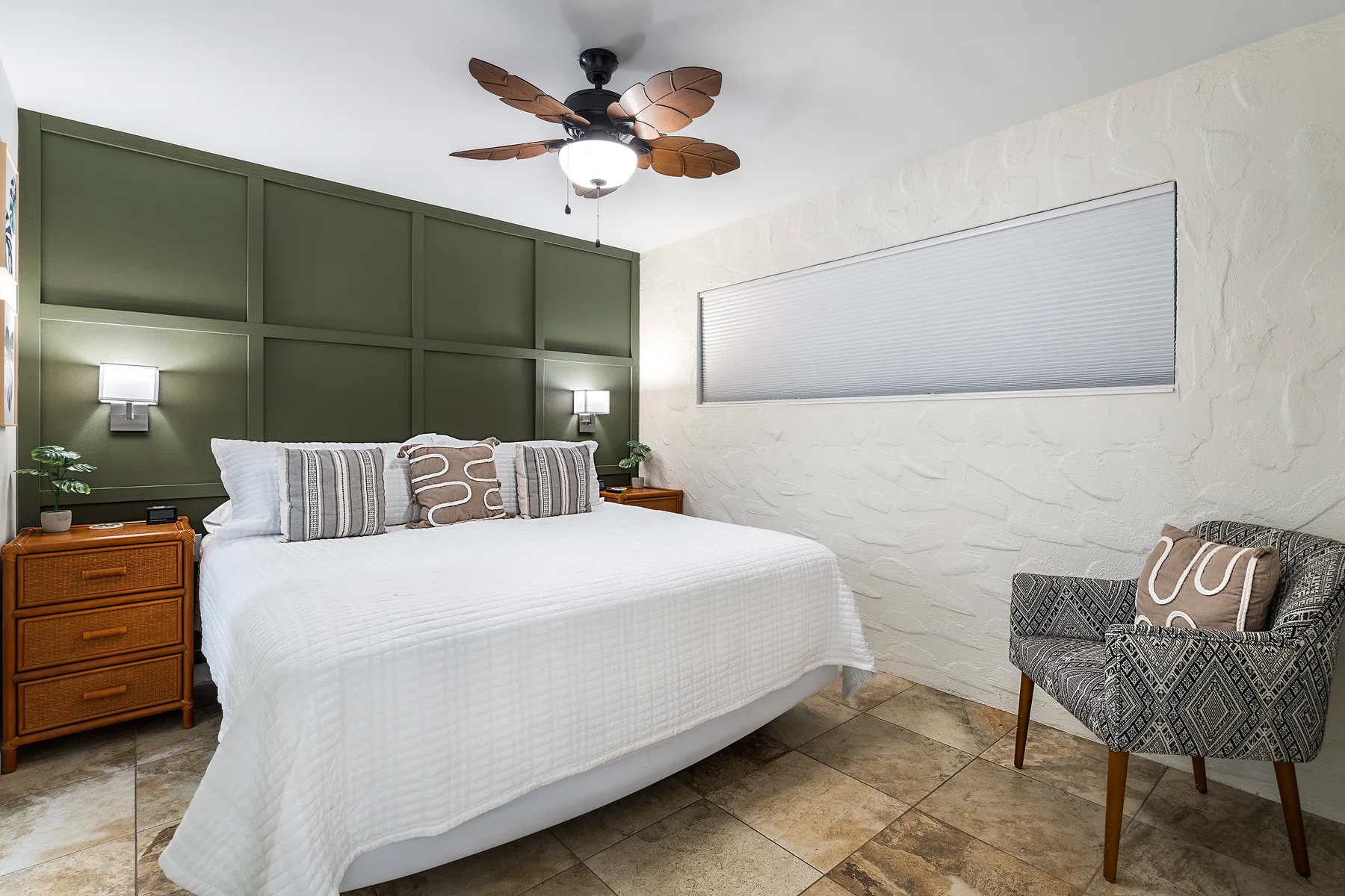 Un dormitorio con una cama blanca, paneles verdes en la pared y un sillón estampado.