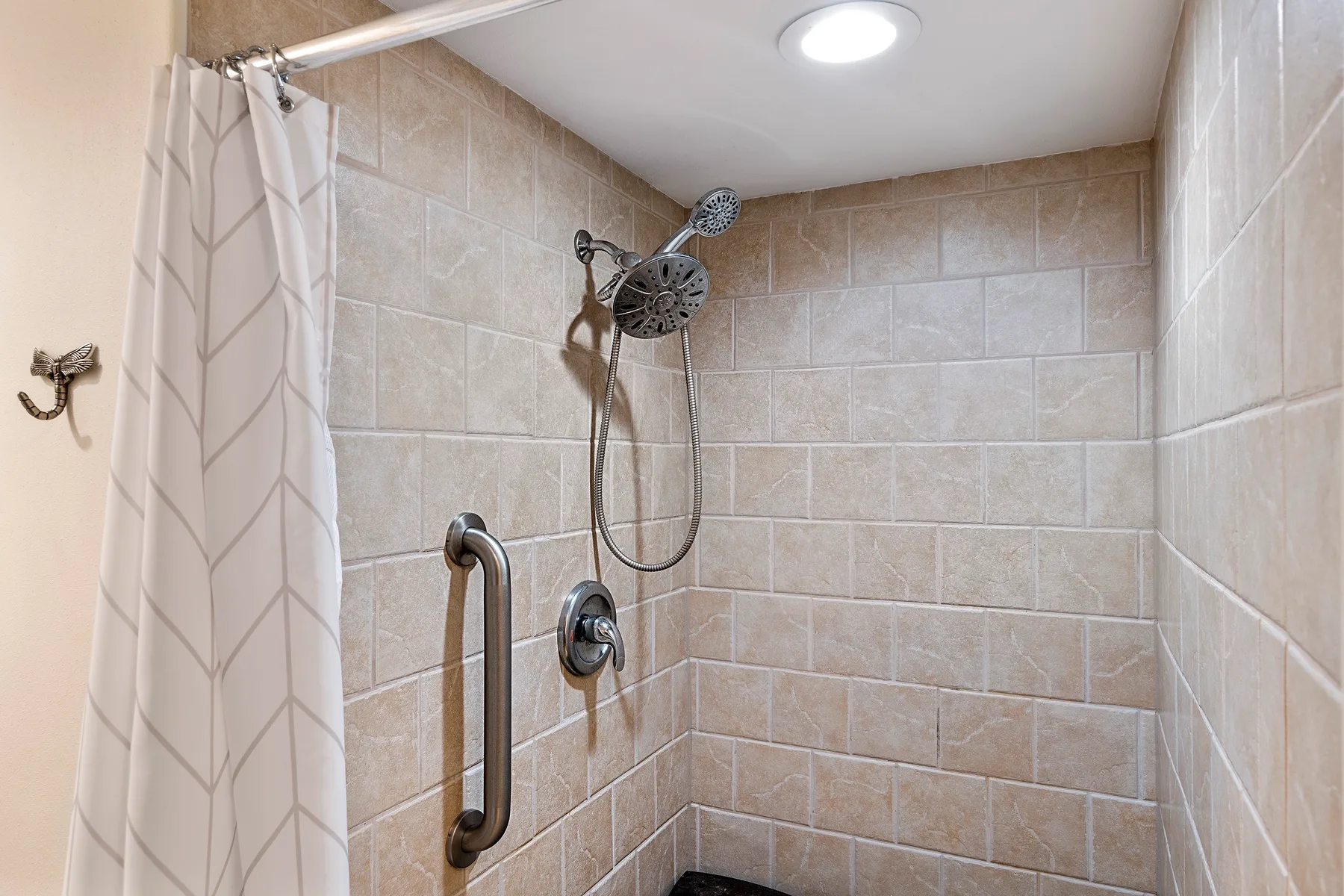 Una ducha con azulejos, ducha de mano y una barra de apoyo.