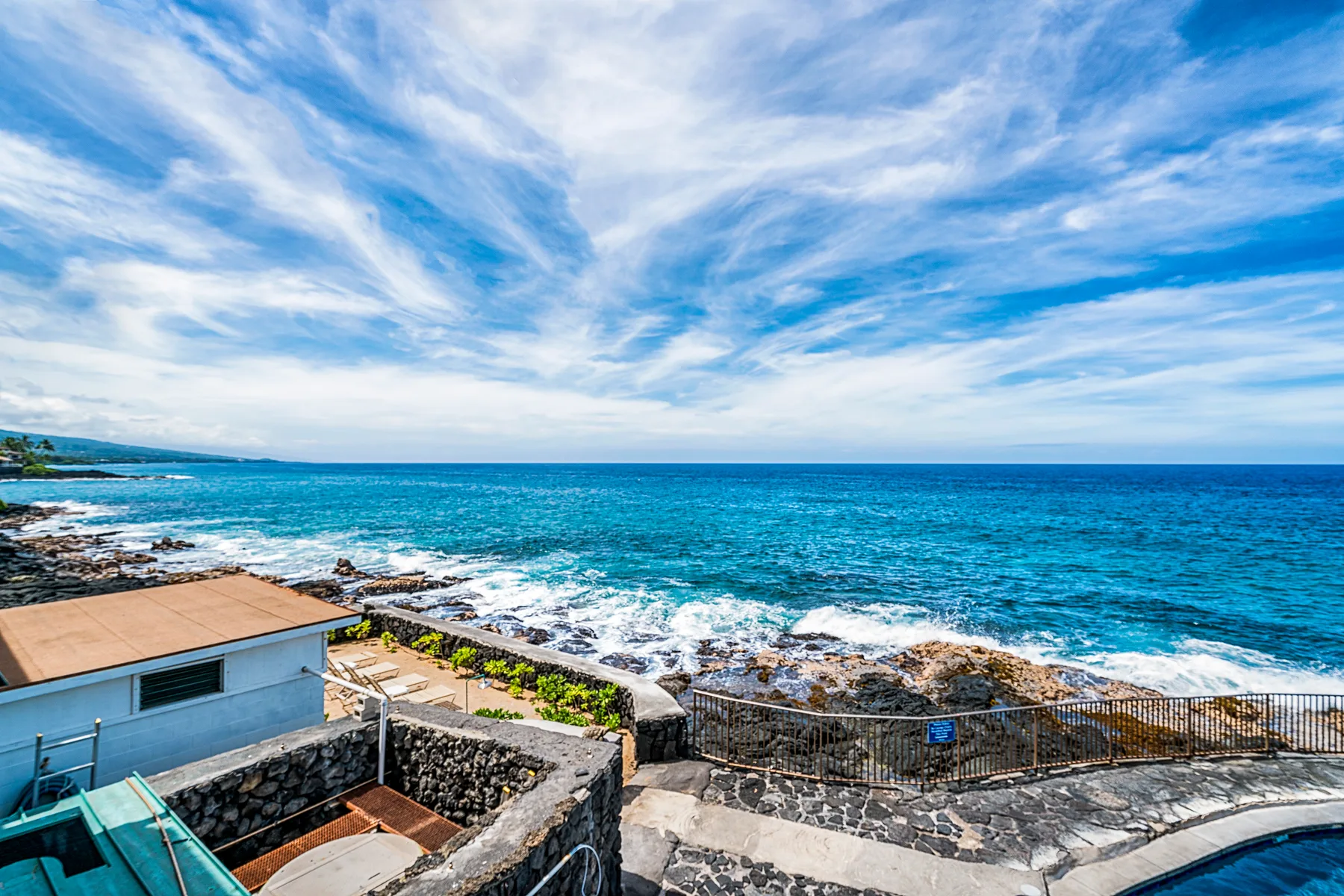Una terraza pavimentada junto al mar mira hacia una costa rocosa y el océano azul.