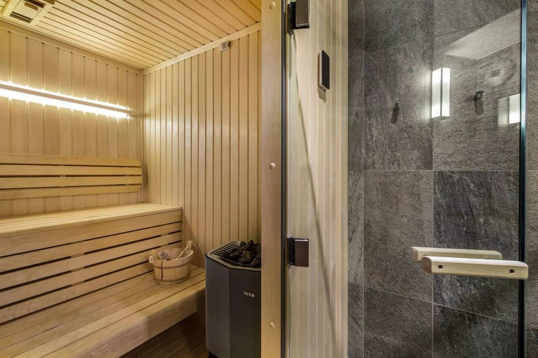 A wooden sauna with tiered seating stands beside a tiled shower.